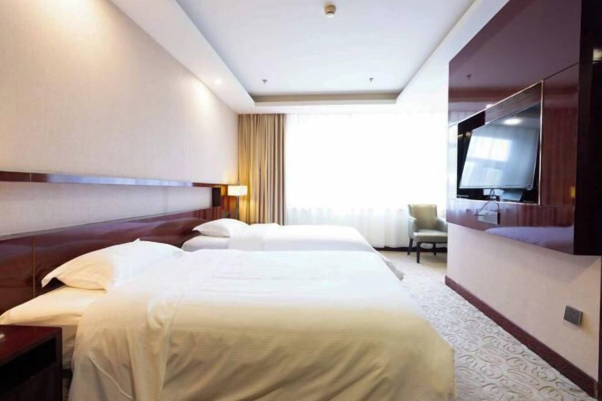 A hotel room with a large bed, a TV mounted on the wall, and a window with curtains.