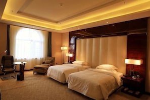 A hotel room with two beds, a desk, a chair, and a lamp.