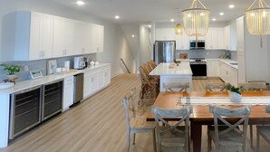 A modern kitchen with white cabinets, a wooden dining table, and two hanging chandeliers. - Ocean block Townhouse with private pool and elevator (Ocean City)