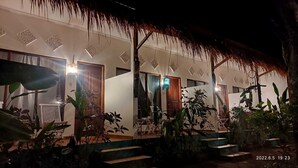 A well-lit building with a thatched roof, surrounded by lush greenery and steps leading to the entrance. - Salty Sea Guesthouse (Jimbaran)