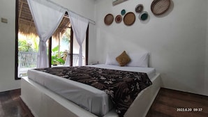 A bedroom with a bed, white curtains, a window with a view of greenery, and decorative plates on the wall. - Salty Sea Guesthouse (Jimbaran)