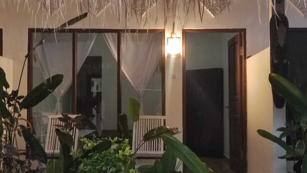 A room with a large sliding glass door, a white railing, and a hanging plant. - Salty Sea Guesthouse (Jimbaran)