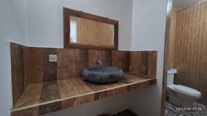 A bathroom with a stone sink, a wooden-framed mirror, and a toilet. - Salty Sea Guesthouse (Jimbaran)
