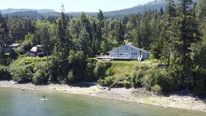 Ein Haus mit einer großen Terrasse mit Blick auf einen Fluss, umgeben von dichtem Wald.