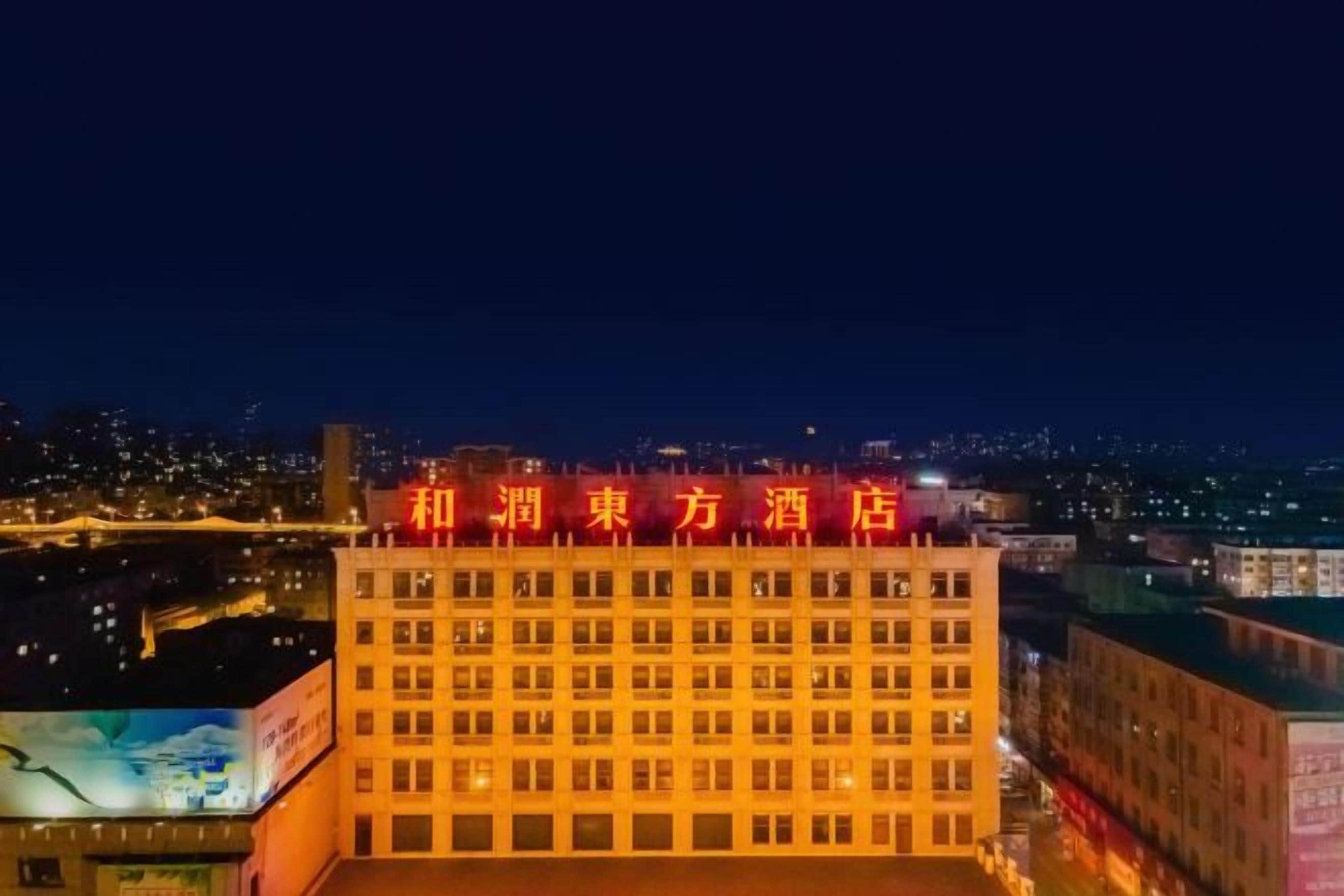 Ein Hotel mit auffälligem roten Schild, mehreren Stockwerken und Blick auf die Stadt im Hintergrund.
