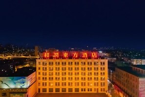 A hotel with a prominent red sign, multiple floors, and a view of the cityscape in the background. - HR-East Hotel (Dalian)