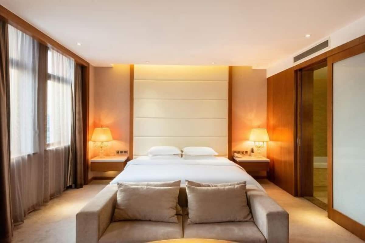 A hotel room with a large bed, two bedside tables with lamps, a sofa, and a sliding door.