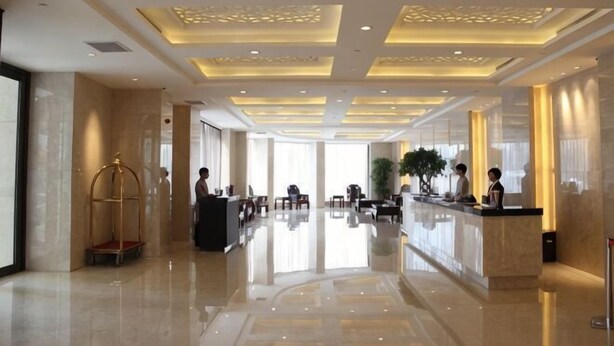 Un vestíbulo de hotel con mostrador de recepción, zona de estar y una planta grande.