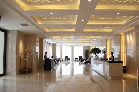 A hotel lobby with a reception desk, seating area, and a large plant.. HR-East Hotel