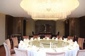 A dining room with a round table set for a meal, surrounded by chairs, and a large chandelier above. - HR-East Hotel (Dalian)