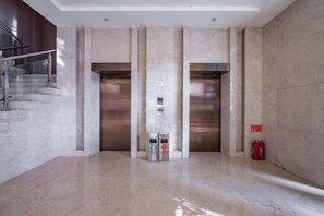 A modern elevator area with a marble floor, two elevators, and a fire extinguisher. - HR-East Hotel (Dalian)