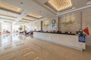 A hotel reception area with a marble counter, a clock, and a flag. - HR-East Hotel (Dalian)