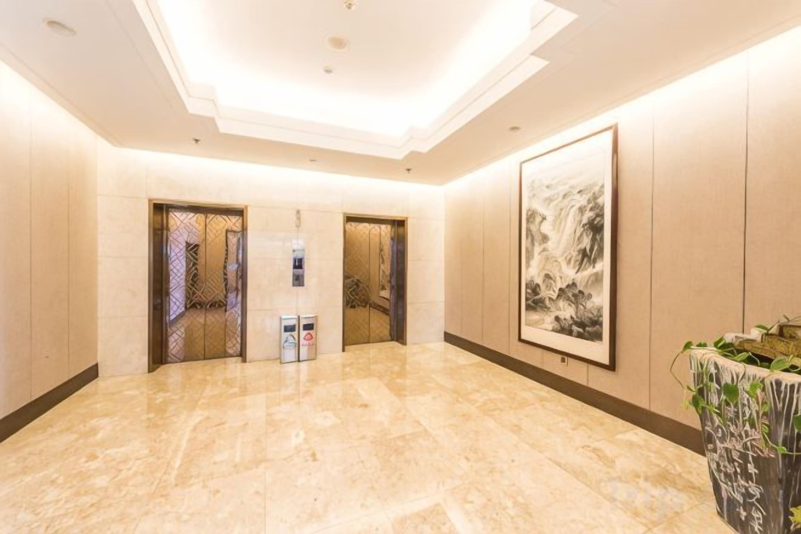 Un vestíbulo de hotel con piso de mármol, dos puertas, una obra de arte enmarcada y una planta en maceta.