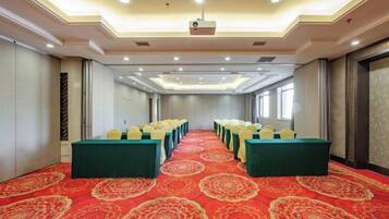 A conference room with rows of tables, a red carpet, and a projector on the ceiling.