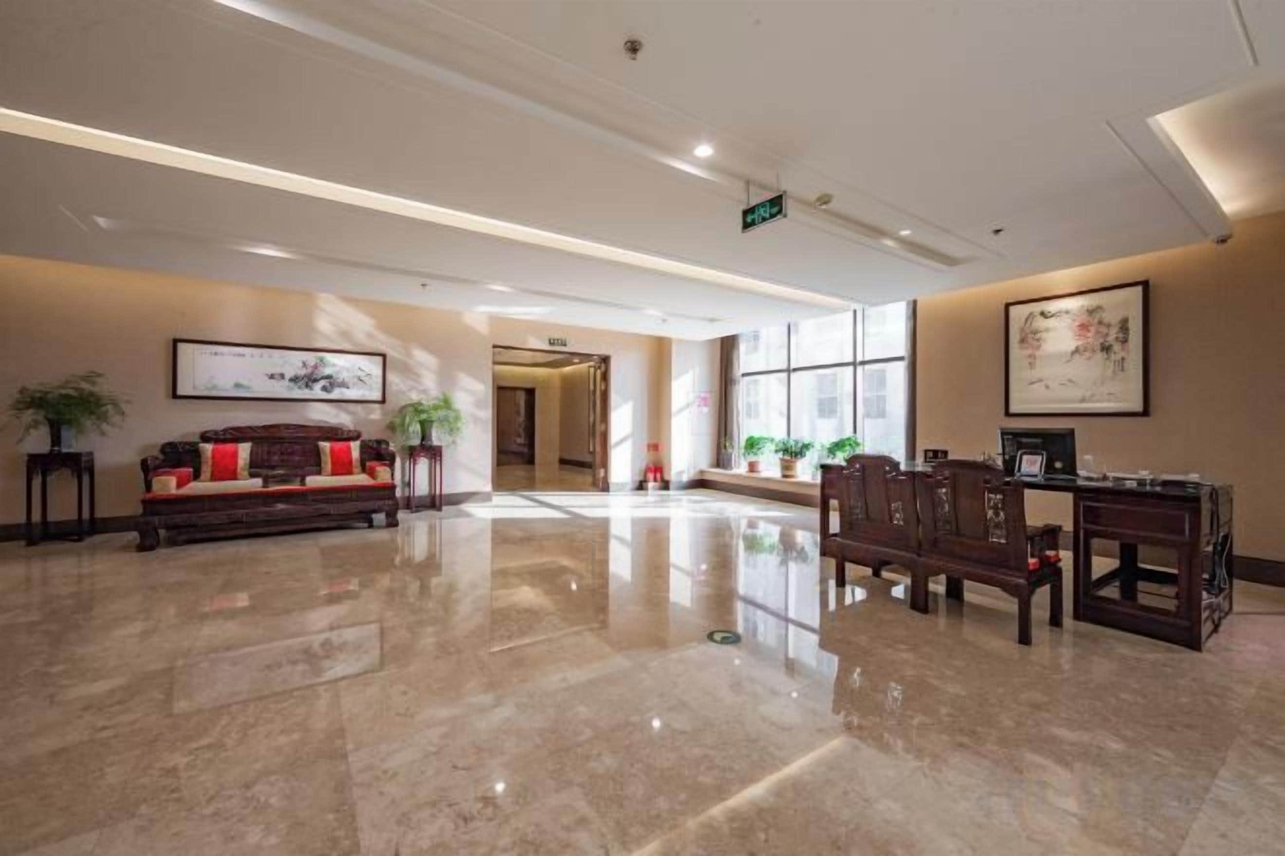 A hotel lobby with a polished marble floor, a reception desk, a sofa, and framed artwork on the walls.