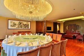 A round dining table set with chairs, a chandelier, and artwork on the walls. - HR-East Hotel (Dalian)