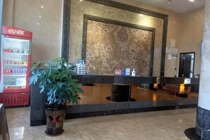 A reception area with a marble wall, a reception desk, a potted plant, and a vending machine. - Shanshui Hotel (Kaiping)