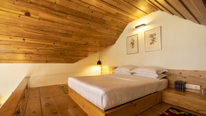 Techo de madera, una cama con ropa de cama blanca, una mesita de noche y dos láminas enmarcadas con motivos botánicos en la pared.