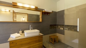 Un baño moderno con tocador de madera, un espejo grande, un lavabo blanco y cabina de ducha con paredes de vidrio.