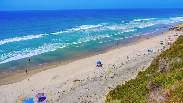 Een strand met helderblauw water, een zandstrand en parasols.