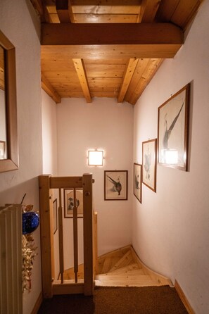 A narrow hallway with wooden beams on the ceiling, a wooden chair, and framed pictures on the walls. - Cesa Monti pallidi 1 - Cesa Monti pallidi (Canazei)