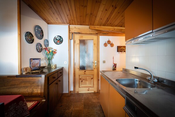 A compact kitchen with wooden cabinets, a stainless steel sink, and a wooden door. - Cesa Monti pallidi 1 - Cesa Monti pallidi (Canazei)