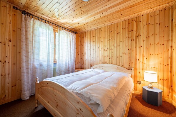 A wooden-paneled room with a bed, curtains, and a bedside lamp. - Cesa Monti pallidi 1 - Cesa Monti pallidi (Canazei)