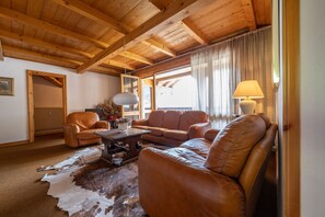 A cozy living room with wooden beams, leather sofas, a coffee table, and a fur rug.