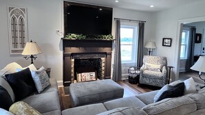 A living room with a fireplace, grey sofas, a patterned armchair, and a television above the fireplace. - 1875 FARMHOUSE renovated with a spectacular view! SUMMER SPECIALS! (Luray)