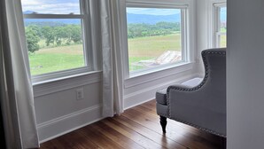 A room with large windows, wooden flooring, and a grey upholstered chair. - 1875 FARMHOUSE renovated with a spectacular view! SUMMER SPECIALS! (Luray)