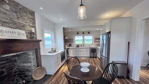 A modern kitchen with white cabinets, a stone accent wall, a wooden dining table with chairs, and a hanging pendant light. - 1875 FARMHOUSE renovated with a spectacular view! SUMMER SPECIALS! (Luray)