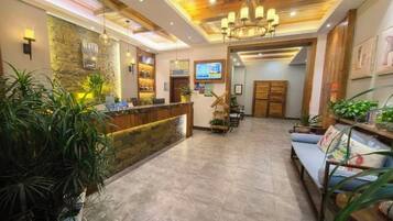 A hotel lobby with a reception desk, seating area, and a chandelier.