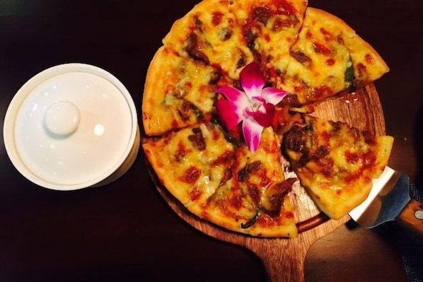 A pizza on a wooden board with a white lid nearby. - Bei'an Theme Hotel (Deqing)