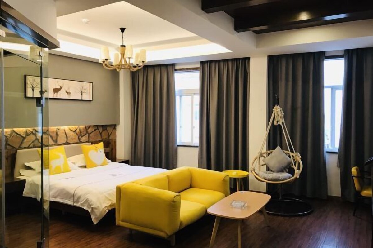 A modern hotel room with a large bed, a yellow sofa, a hanging chair, and a small table.