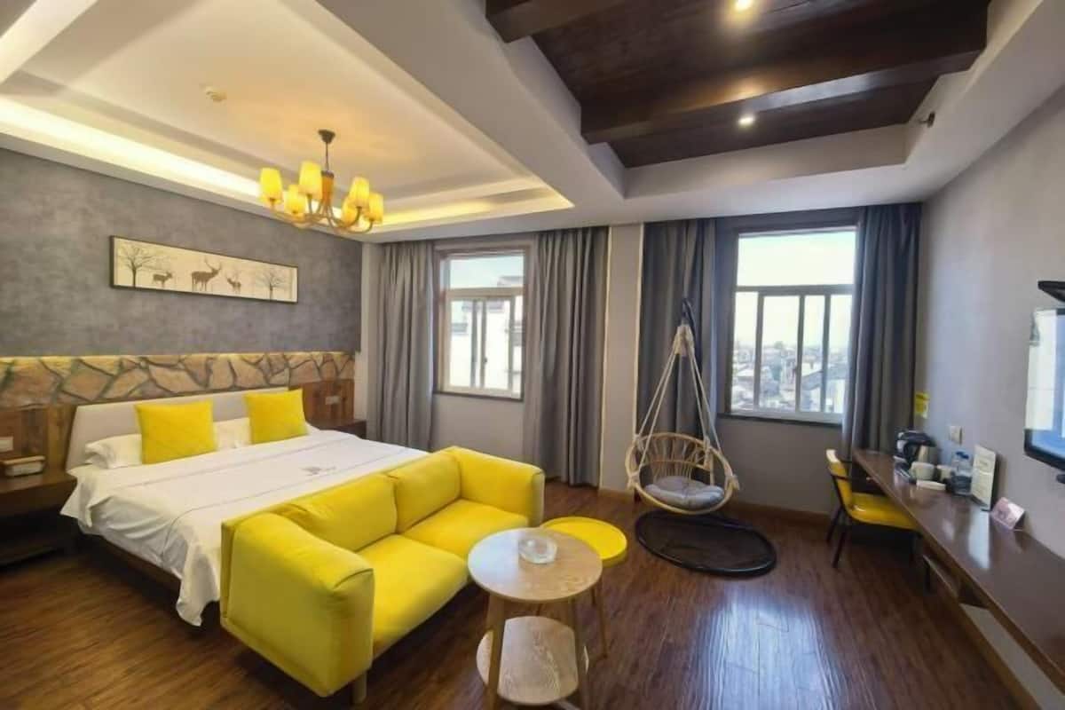 Une chambre d’hôtel avec un lit, un canapé jaune, une petite table ronde, un fauteuil suspendu et un bureau avec une chaise.