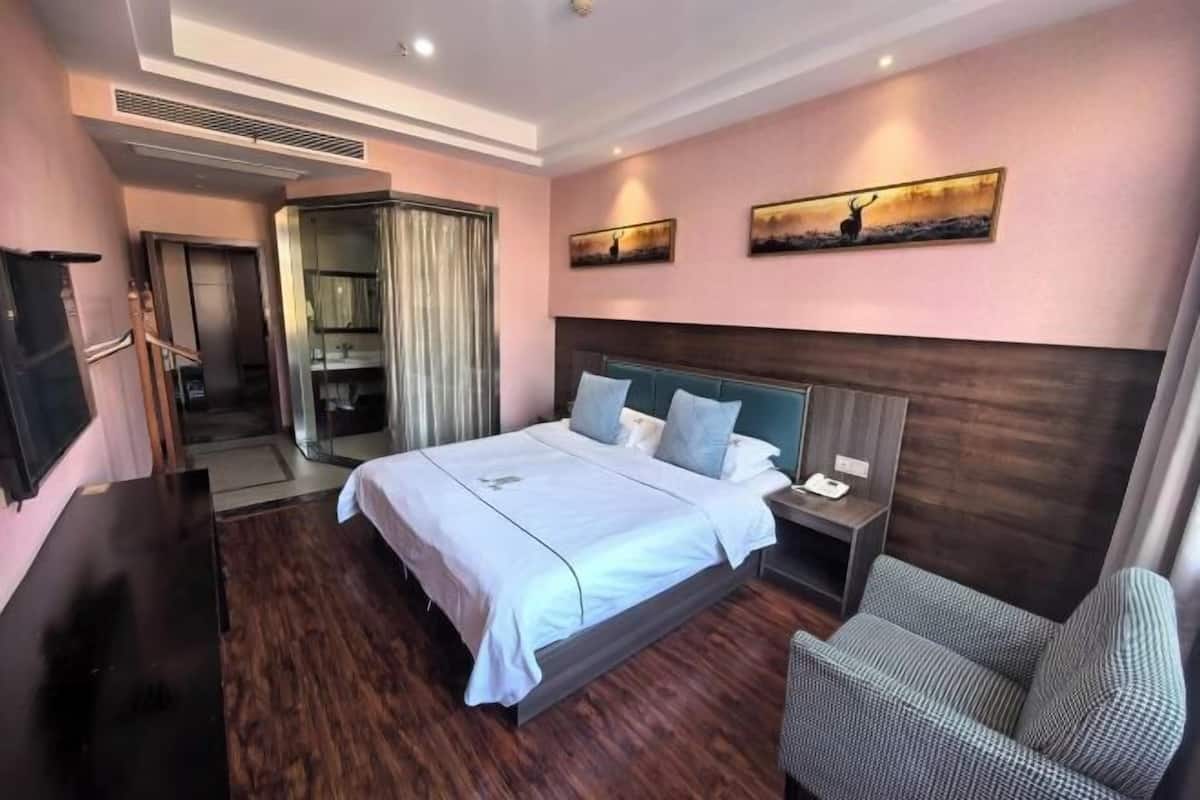Une chambre d’hôtel avec un grand lit, un bureau, une chaise, une télévision et une salle de bain équipée d’une douche et de toilettes.