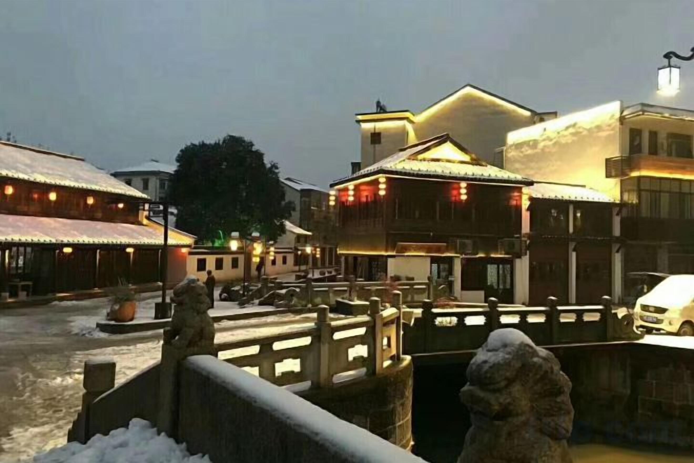A traditional building with a wooden facade, a stone bridge, and a snow-covered ground.