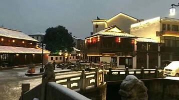 A traditional building with a wooden facade, a stone bridge, and a snow-covered ground.
