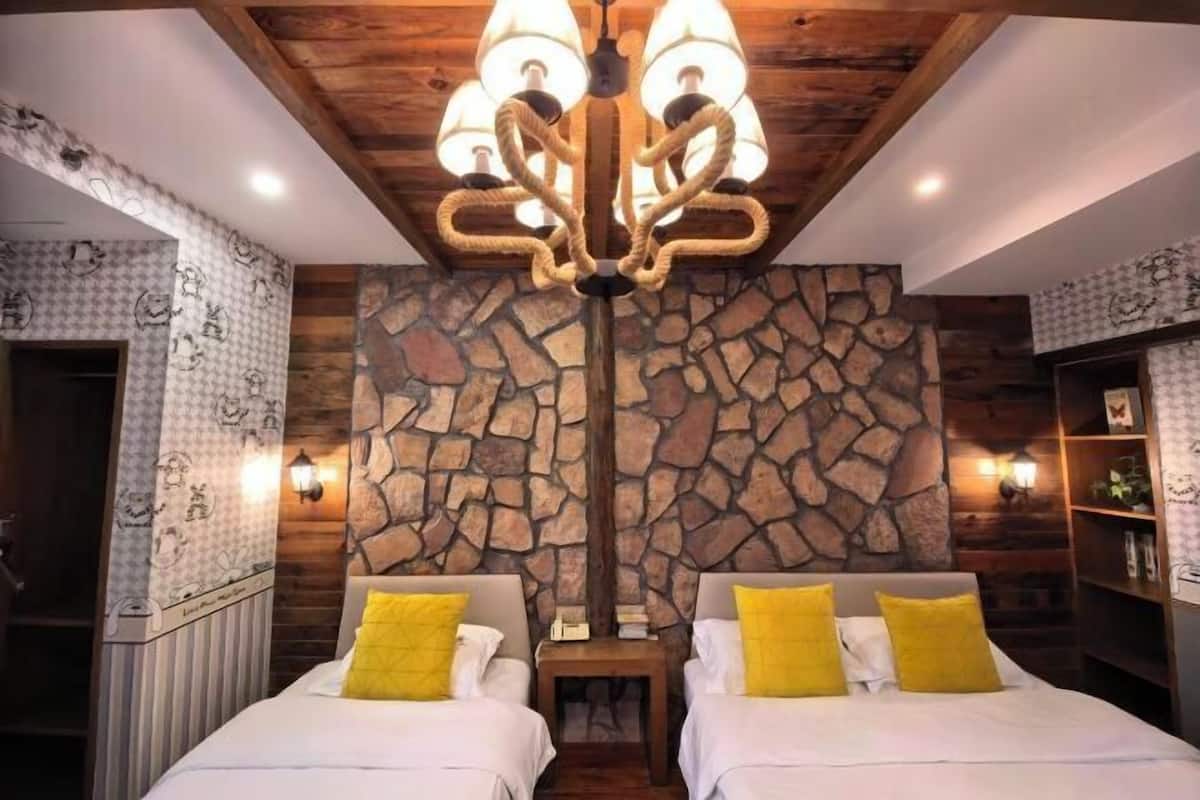 Une pièce avec un mur en pierre, deux lits avec des oreillers jaunes, un plafond en bois et un lustre.