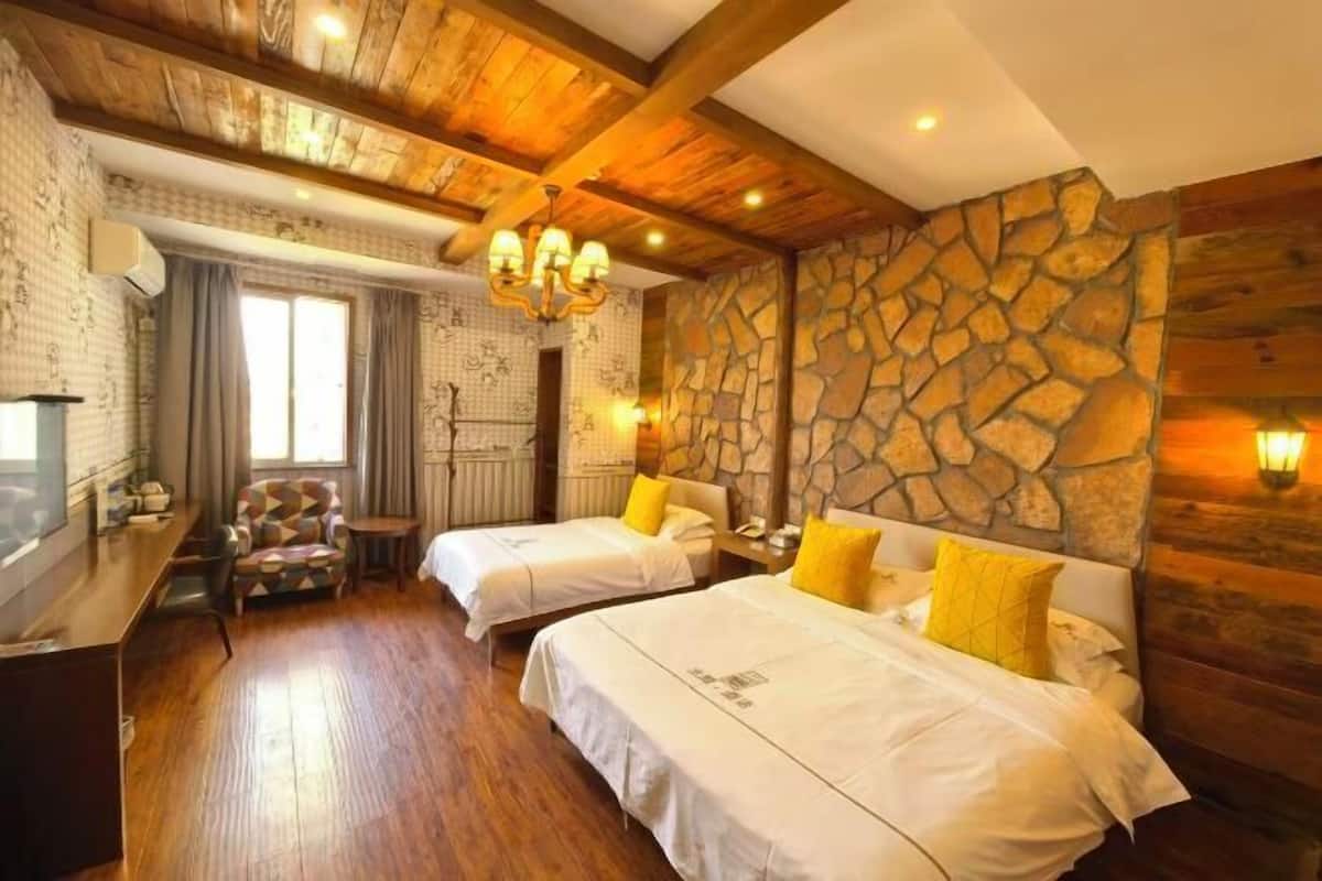 Une chambre avec deux lits, un plancher en bois, un mur en pierre, un lustre et une petite table avec des chaises.