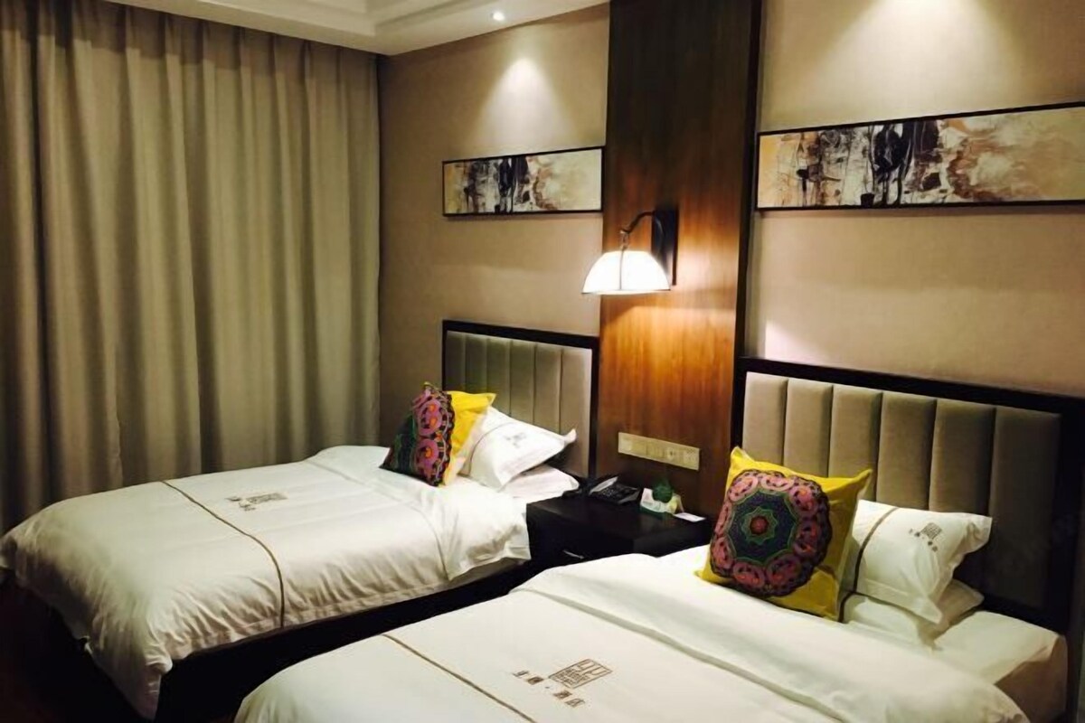 A hotel room with two beds, a nightstand, a lamp, and artwork on the walls.