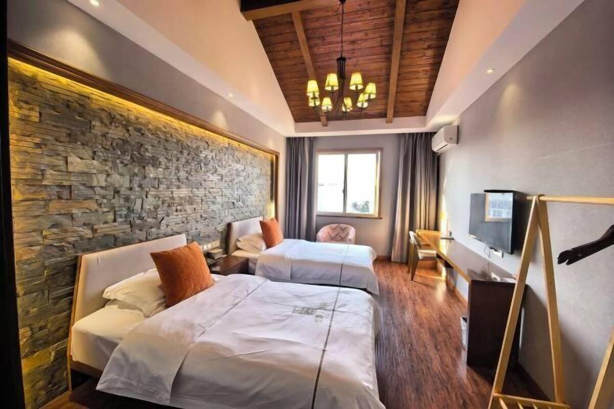 Une chambre d’hôtel avec deux lits, un mur en pierre, un plafond en bois et une télévision.