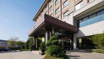 A modern hotel entrance with a covered walkway, large windows, and a landscaped area with shrubs.
