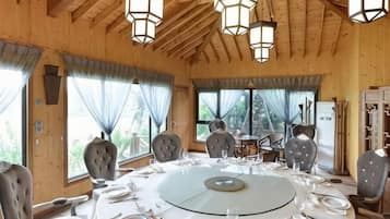 A dining area with a round table set for six, surrounded by chairs, in a room with wooden walls and a high ceiling.