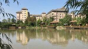 A hotel with multiple buildings, a calm lake, and surrounding greenery. - Oriental Hotel (Taicang)