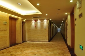 Un pasillo de hotel con puertas de madera, alfombra estampada y una larga galería con iluminación en el techo.