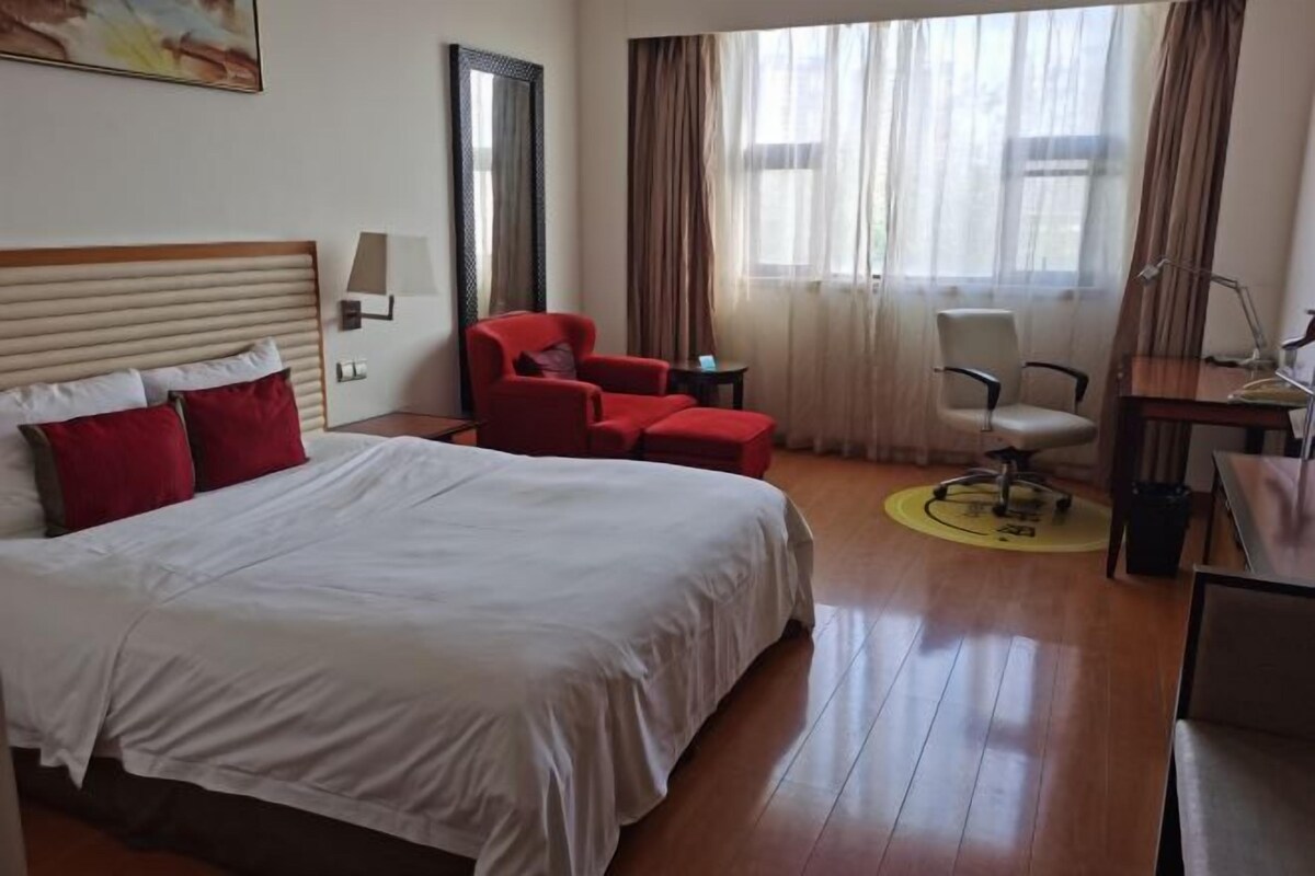 Una habitación de hotel con una cama grande, un escritorio, una silla y una ventana con cortinas.