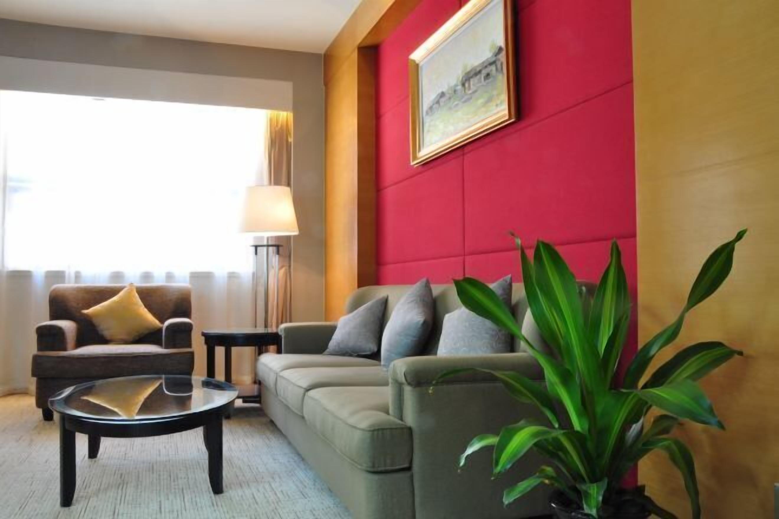 Ein modernes Wohnzimmer mit einer Couch, einem Sessel und einem Couchtisch. Es gibt eine Lampe, ein gerahmtes Bild an der Wand und einen Blumentopf.
