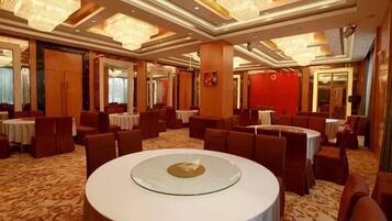 A hotel dining area with round tables, high ceilings, and chandeliers.