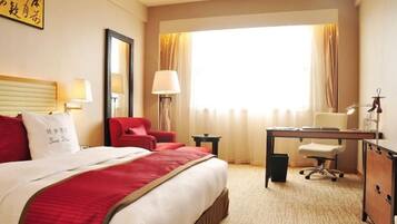 Een hotelkamer met een bed, een bureau, een stoel, een lamp en een raam met gordijnen.